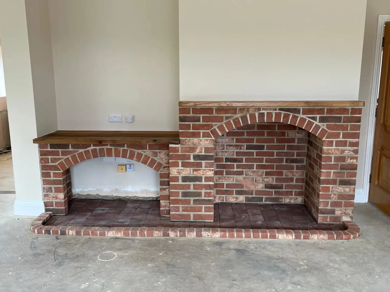 Bespoke brick fire surround with arched openings, a timber mantel and a tiled hearth, built into a renovated lounge
